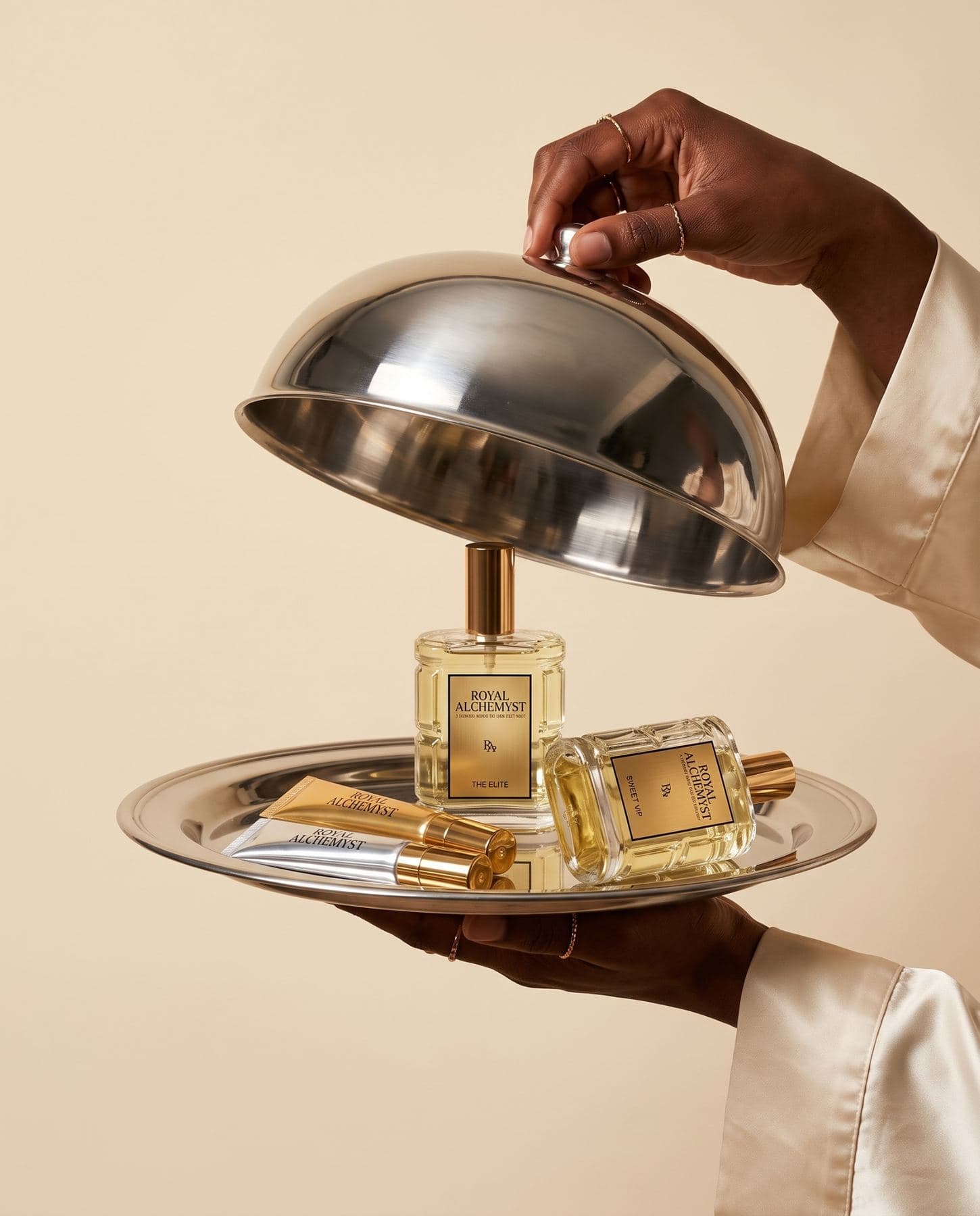 A hand lifting a silver cloche from a tray of Royal Alchemyst body oils